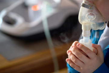 Child makes inhalation at home with nebulizer on out of focus background. Example of combating respiratory diseases such as tracheitis bronchitis pneumonia with medical equipment at home conditions - obrazy, fototapety, plakaty