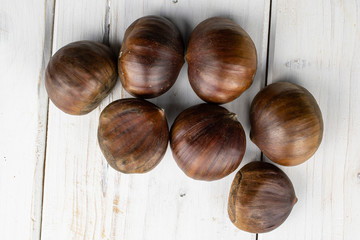Group of seven whole edible brown chestnut flatlay on white wood