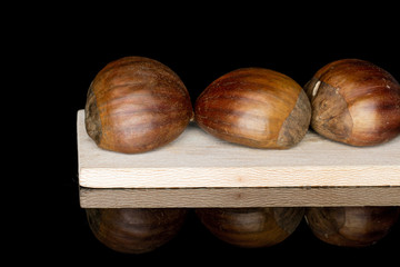 Group of three whole edible brown chestnut on wooden cutting board isolated on black glass