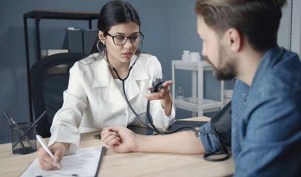 Woman physician measuring patient's blood pressure and writing it down to medical record