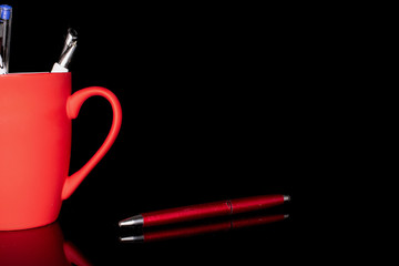 Group of three whole writing ballpoint pen one separated with red ceramic cup isolated on black...