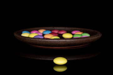 Obraz na płótnie Canvas Lot of whole sweet colourful candy yellow in front with brown ceramic coaster isolated on black glass