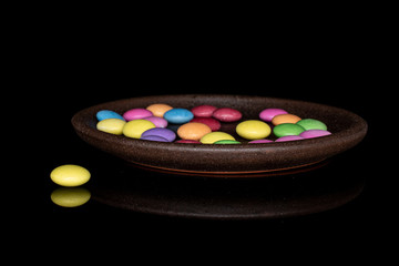 Lot of whole sweet colourful candy with brown ceramic coaster isolated on black glass