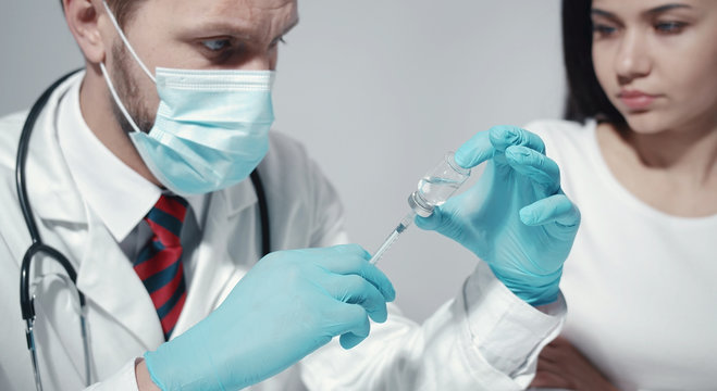Male doctor in medical face mask rubber gloves preparing syringe for waiting patient, cropped image