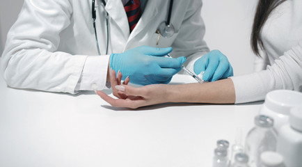 Close-up of doctor's hands in blue latex gloves making injection to female patient's forearm