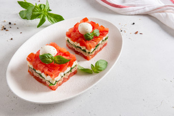 Portioned tuna salad with tomatoes, basil and mozarella on white plate on light background. Healthy nutrition, dieting, keto diet. Side view, copy space. Menu, recipe