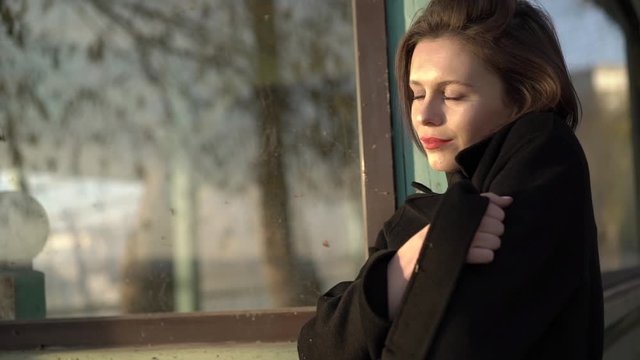 Portrait of seductive brunette wraps herself into coat and poses at house