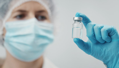 Closeup of medical doctor holding vaccine in transparent glass vial between fingers, focus on bottle