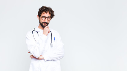 young doctor man looking serious, confused, uncertain and thoughtful, doubting among options or...