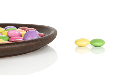 Lot of whole sweet colourful candy with brown ceramic coaster isolated on white background