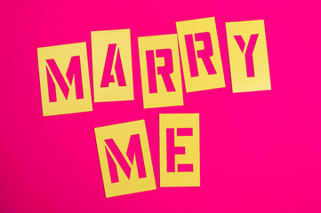 Marry Me message spelled out in yellow stencil lettering on bright pink background