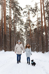 Fototapeta na wymiar happy couple in love in warm jackets walking with their pet, with a dog, in the snow forest in winter, family trip