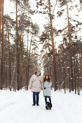 happy couple in love in warm jackets walking with their pet, with a dog, in the snow forest in winter, family trip
