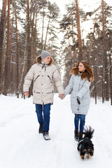 Fototapeta na wymiar happy couple in love in warm jackets walking with their pet, with a dog, in the snow forest in winter, family trip
