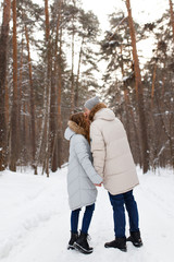 Fototapeta premium Happy lovers a guy and a girl who love each other hug, kiss, laugh, rage and walk in warm jackets in winter against the background of a snowy forest, a friendly family fun walk