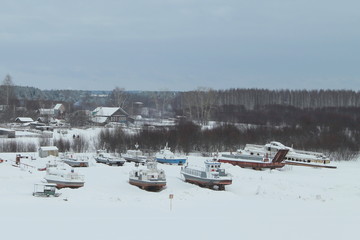 Snow covered landing stage with ships on background of wooden houses and forest