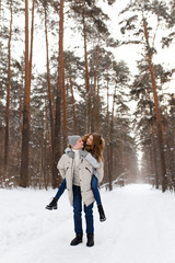 Fototapeta na wymiar Happy lovers a guy and a girl who love each other hug, kiss, laugh, rage and walk in warm jackets in winter against the background of a snowy forest, a friendly family fun walk