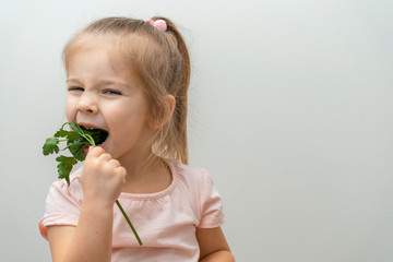little girl squinting and laughing bites off a sprig of parsley