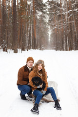 Obraz premium happy couple in love in warm jackets walking with their pet, with a dog, in the snow forest in winter, family trip