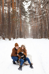 Obraz premium happy couple in love in warm jackets walking with their pet, with a dog, in the snow forest in winter, family trip