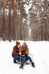 Fototapeta premium happy couple in love in warm jackets walking with their pet, with a dog, in the snow forest in winter, family trip