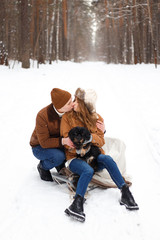 Fototapeta premium happy couple in love in warm jackets walking with their pet, with a dog, in the snow forest in winter, family trip