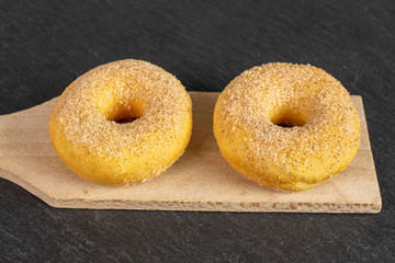 Group of two whole sweet golden mini cinnamon donut on small wooden cutting board on grey stone