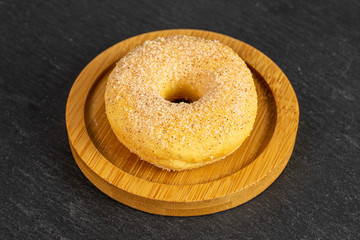 One whole sweet golden mini cinnamon donut on bamboo coaster on grey stone