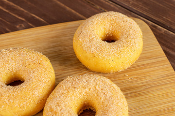 Group of three whole sweet golden mini cinnamon donut on bamboo cutting board on brown wood
