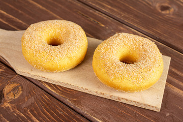 Group of two whole sweet golden mini cinnamon donut on small wooden cutting board on brown wood