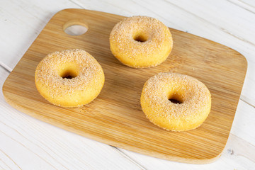 Group of three whole sweet golden mini cinnamon donut on bamboo cutting board on white wood