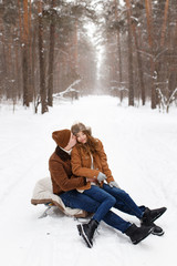 Fototapeta premium Happy lovers a guy and a girl who love each other hug, kiss, laugh, rage and walk in warm jackets in winter against the background of a snowy forest, a friendly family fun walk