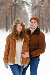 Happy lovers a guy and a girl who love each other hug, kiss, laugh, rage and walk in warm jackets in winter against the background of a snowy forest, a friendly family fun walk