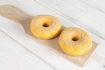 Group of two whole sweet golden mini cinnamon donut on small wooden cutting board on brown wood