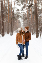 Happy lovers a guy and a girl who love each other hug, kiss, laugh, rage and walk in warm jackets in winter against the background of a snowy forest, a friendly family fun walk