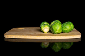 Group of four whole fresh green brussels sprout on bamboo cutting board isolated on black glass