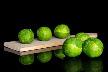 Group of six whole fresh green brussels sprout on small wooden cutting board isolated on black glass