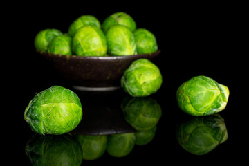 Lot of whole fresh green brussels sprout in dark ceramic bowl isolated on black glass