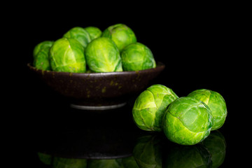 Group of nine whole fresh green brussels sprout in dark ceramic bowl isolated on black glass