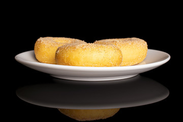 Group of three whole sweet golden mini cinnamon donut on white ceramic plate isolated on black glass