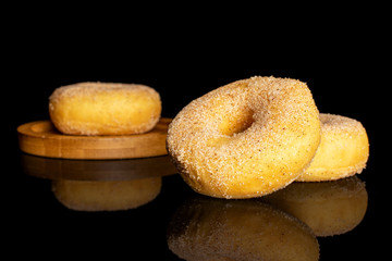 Group of three whole sweet golden mini cinnamon donut on bamboo coaster isolated on black glass
