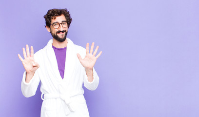 young bearded man wearing bathrobe smiling and looking friendly, showing number nine or ninth with...