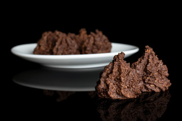 Group of six whole homemade brown coconut cocoa biscuit on white ceramic plate isolated on black glass