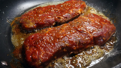Marinated beef steaks in grease on frying pan.