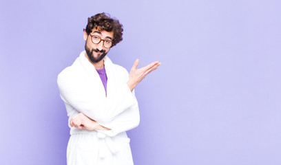 young bearded man wearing bathrobe feeling confused and clueless, wondering about a doubtful...