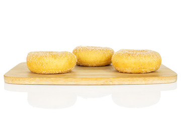 Group of three whole sweet golden mini cinnamon donut on bamboo cutting board isolated on white background