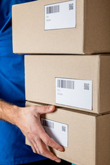 Cropped view of delivery man in uniform holding cardboard packages with qr codes and barcodes on cards