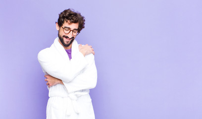 young bearded man wearing bathrobe feeling in love, smiling, cuddling and hugging self, staying...