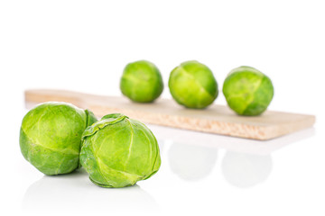 Group of five whole fresh green brussels sprout on small wooden cutting board isolated on white background