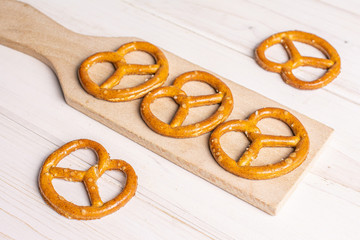 Group of five whole salty brown pretzel on small wooden cutting board on white wood